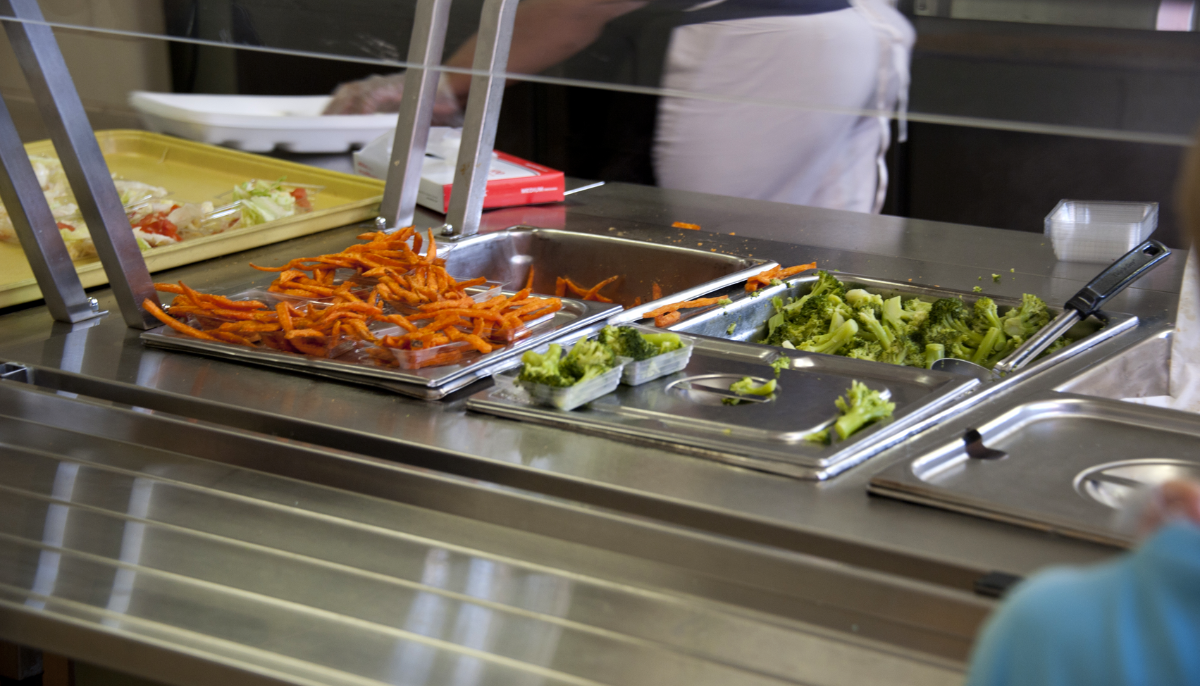 Various vegetables being cooked in a cafeteria setting